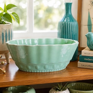 May include: A light mint green ceramic bowl with a scalloped rim and a decorative embossed dot pattern around the base. The bowl features a glossy finish with subtle white distressed accents along the fluted sides, creating a textured appearance.