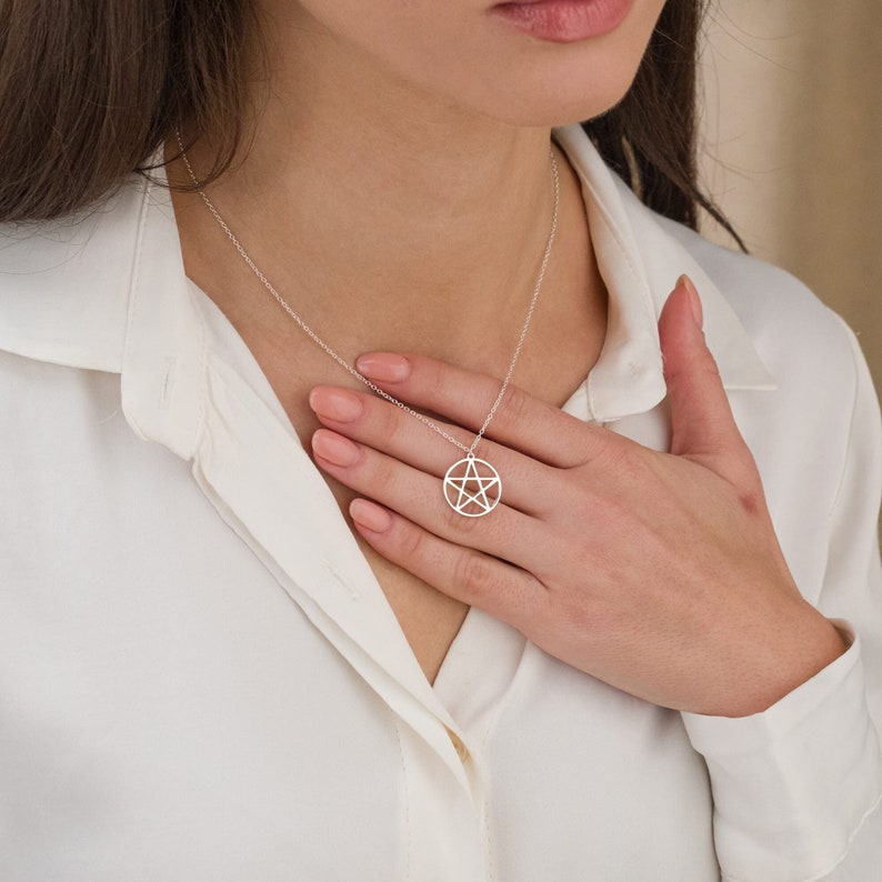 May include: Silver necklace featuring a circular pendant with a pentagram design. The chain is delicate and the pendant is simple yet elegant.  The minimalist style makes it a versatile piece of jewelry suitable for everyday wear or special occasions.  The pendant is a subtle yet eye-catching statement piece.