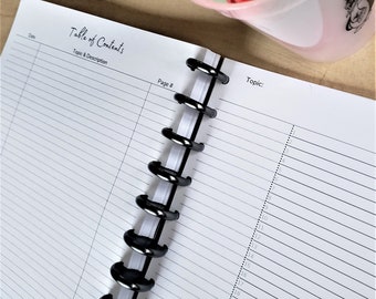 May include: A white notebook with black lines and a black spiral binding. The notebook has the words "Table of Contents" and "Topic & Description" printed on the cover. The notebook is open to a page with the words "Page #" and "Topic" printed at the top.