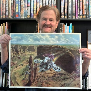 Puede incluir: Una ilustración en color de un vehículo futurista volando sobre un paisaje desértico. El vehículo es una motocicleta con dos grandes hélices en la parte trasera y dos más pequeñas en los laterales. El conductor lleva una chaqueta de cuero y un casco. La ilustración está firmada por el artista y fechada en 2002.