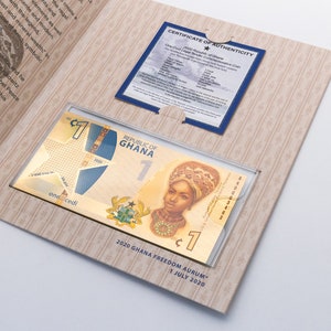 May include: A gold-plated 1 Ghanaian cedi banknote in a clear plastic sleeve. The banknote features a portrait of a woman wearing a traditional head covering and a gold necklace. The text "Republic of Ghana" and "2020 Ghana Freedom Aurum - 1 July 2020" is printed on the banknote.