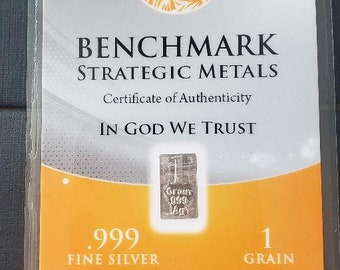 May include: A certificate of authenticity for a 1-grain .999 fine silver bar. The certificate features a depiction of the Statue of Liberty and the text "BENCHMARK STRATEGIC METALS" and "IN GOD WE TRUST". The certificate is a proud member of the Jewelers Vigilance Committee.