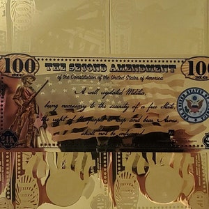 May include: A gold-coloured paper bill with the text "The Second Amendment of the Constitution of the United States of America" and "A well regulated Militia, being necessary to the security of a free State, the right of the people to keep and bear Arms, shall not be infringed". The bill also features a portrait of a man holding a rifle and the text "100 MG" on both sides.