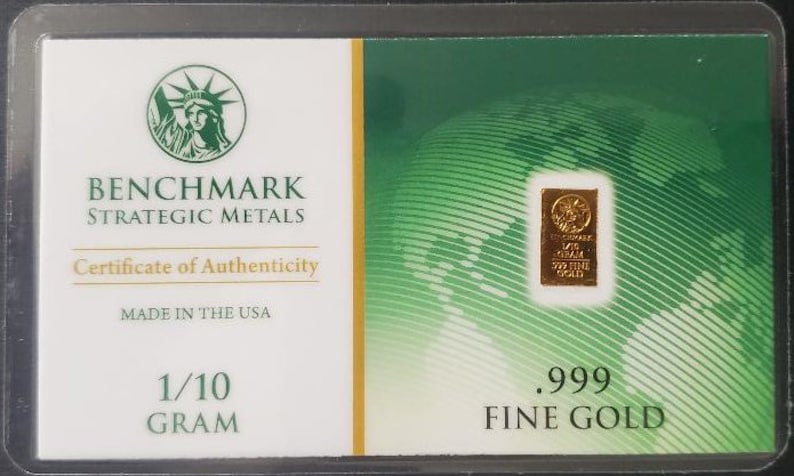 Puede incluir: Un certificado de autenticidad para una barra de oro fino de 0,1 gramos a 999 mil&eacute;simas. El certificado presenta un fondo verde con un dise&ntilde;o de globo terr&aacute;queo y el texto "BENCHMARK STRATEGIC METALS".