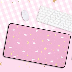 Peut inclure: Tapis de souris rose avec une bordure blanche et un motif répétitif de nuages blancs, d'étoiles jaunes et de croissants de lune. Le tapis de souris est sur une surface à carreaux rose et blanche.