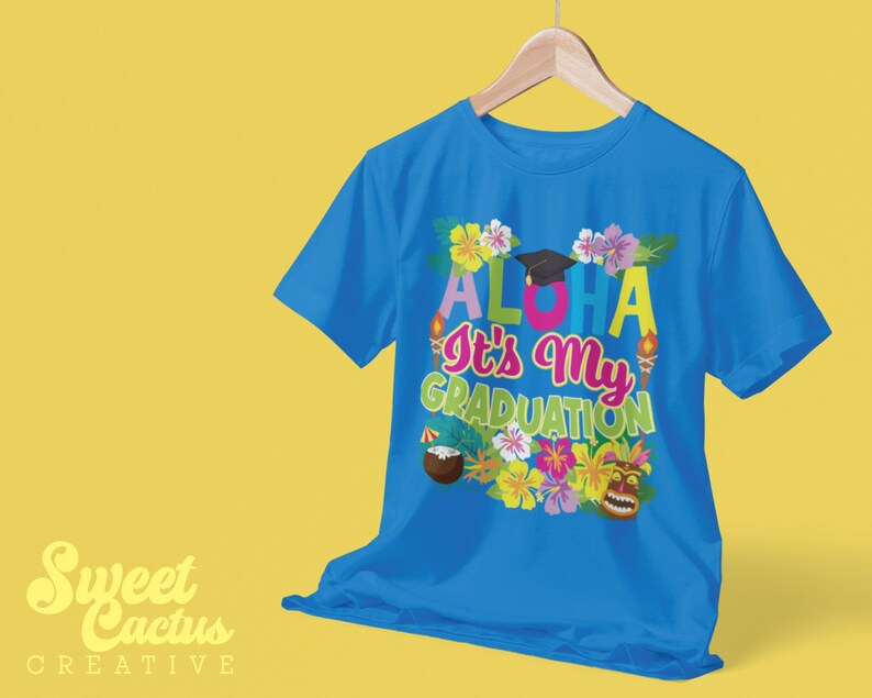 May include: A blue t-shirt with a colorful design that says "Aloha It's My Graduation" with a graduation cap, flowers, and a tiki mask.