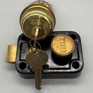 May include: A vintage lock set featuring a brass cylinder lock with the word "SAFE" and a key, a black rectangular lock body, and a brass circular cover with the word "EAGLE". The set is designed for security and access control.