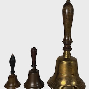 May include: Three antique bells of varying sizes. The smallest has a black handle, the middle one a brown handle, and the largest a long, ornate wooden handle. All bells have a brass finish.