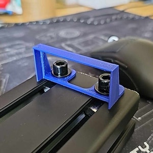 May include: A blue 3D printed bracket with two black screws. The bracket is attached to a black metal track.