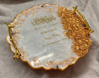 May include: A white and gold round serving tray with a decorative gold branch handle. The tray has gold leaf accents and the text "Basmala" in Arabic script, "Ayan & Eshal", "21 March 2023", "Tukhlifna kam azwaj", and "And we created you in pairs".