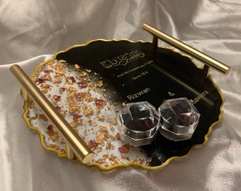 Könnte beinhalten: Ein schwarzes und weißes Harztablett mit goldenen Akzenten und einem goldenen Griff. Das Tablett hat eine weiße und goldene Seite mit roten und goldenen Flocken und eine schwarze Seite mit goldenen Buchstaben. Die Beschriftung lautet "And We Created You in Pairs Quran 76:8 Rizwan & Sawera". Das Tablett hat zwei kleine transparente Boxen mit schwarzen Deckeln.