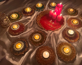Könnte beinhalten: Ein rotes Harztablett mit goldenen Akzenten und dem Text "Fatima Mehndi" in Weiß. Das Tablett ist von 12 kleinen goldenen und roten Kerzenhaltern mit brennenden Teelichtern umgeben.
