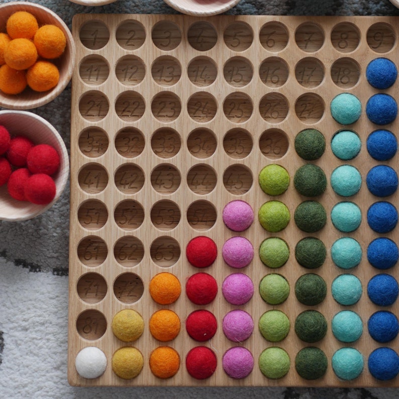May include: A wooden board with numbered circles, filled with colourful felt balls in a rainbow pattern. The board is used for counting and learning maths.