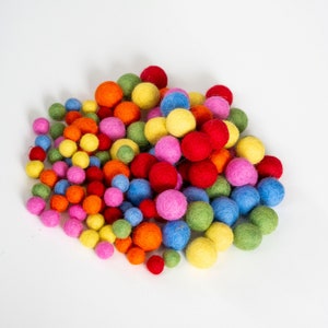 Op de afbeelding: Een grote stapel kleurrijke viltballen in verschillende tinten rood, oranje, geel, groen, blauw en roze. De ballen zijn in een willekeurig patroon gerangschikt en zijn allemaal ongeveer even groot.