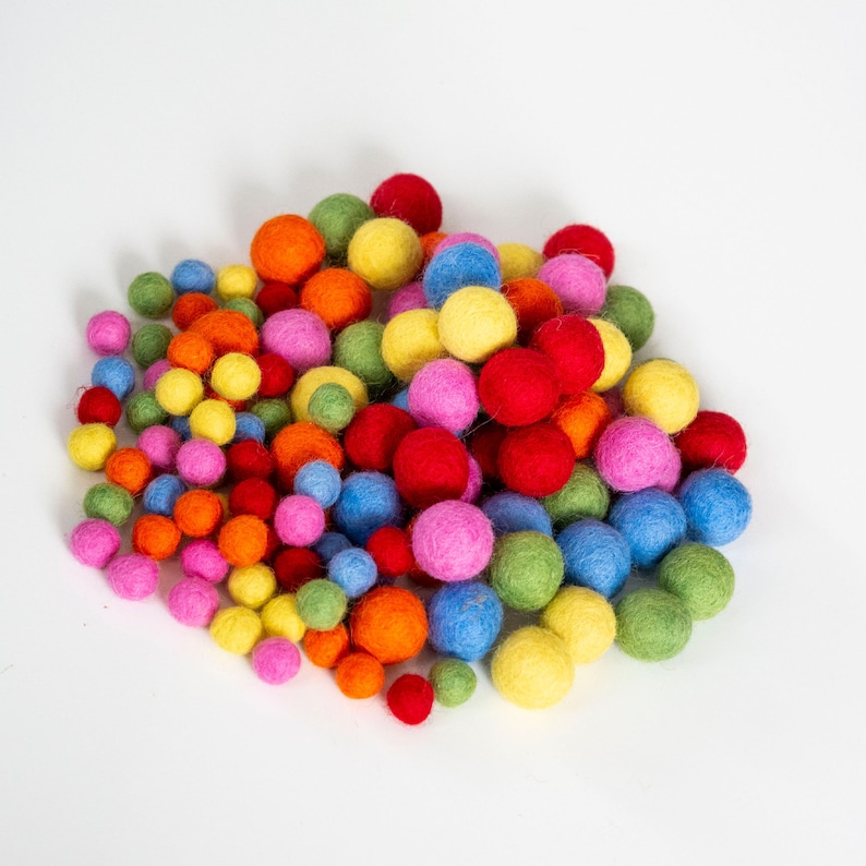 Op de afbeelding: Een grote stapel kleurrijke viltballen in verschillende tinten rood, oranje, geel, groen, blauw en roze. De ballen zijn in een willekeurig patroon gerangschikt en zijn allemaal ongeveer even groot.
