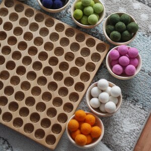 May include: A wooden counting board with numbered circles, surrounded by bowls of colourful felt balls. The bowls contain green, white, pink, orange, and blue felt balls.