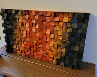May include: A wall art piece made of wood blocks in shades of orange, red, and black. The blocks are arranged in a geometric pattern, creating a gradient effect.