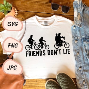 Może przedstawiać: Biała koszulka z czarną sylwetką trzech postaci jadących na rowerach. Pod postaciami nadrukowany jest tekst "FRIENDS DON'T LIE".