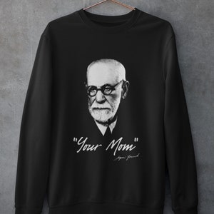 May include: Black sweatshirt featuring a black and white portrait of Sigmund Freud with the text "Your Mom" and his signature in white. The sweatshirt is hanging on a copper-colored hanger.