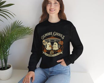 May include: Black sweatshirt with the text "Gilmore Ghouls" and a graphic of two cartoon ghosts in a gazebo. The design includes fall leaves and the phrase "Where you haunt, I will follow."