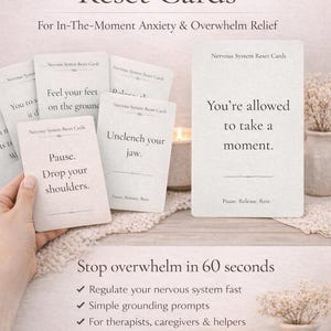 May include: A set of off-white Nervous System Reset Cards featuring black text prompts like You're allowed to take a moment, Pause. Drop your shoulders, and Unclench your jaw. The cards are displayed with a lit candle and dried flowers.
