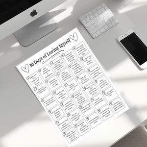 May include: A white paper titled "30 Days of Loving Myself" with a list of self-care prompts. The paper is on a white desk with a computer, keyboard, and phone. The prompts include "Speak one kind sentence to yourself today" and "Commit to treating yourself with kindness."