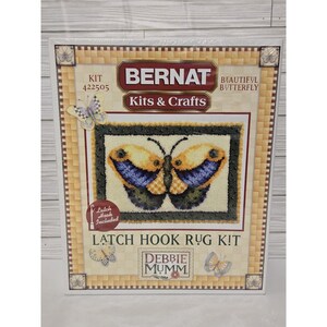 May include: A Bernat latch hook rug kit featuring a butterfly design. The kit includes a rug canvas with a butterfly pattern in yellow, blue, and black. The packaging includes the text "Beautiful Butterfly" and "Debbie Mumm".
