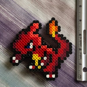 Puede incluir: Arte de cuentas de perler rojo, naranja, amarillo, blanco y negro de un personaje de dibujos animados. El personaje es un dragón rojo con la barriga amarilla y los ojos blancos.