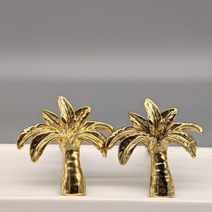 Könnte beinhalten: Zwei goldene, palmenförmige, dekorative Schubladenknöpfe.