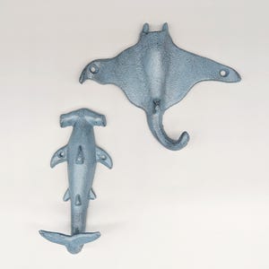以下が含まれることがあります： 海洋生物の形をした鋳鉄製の壁掛けフック2つ。 一つはシュモクザメ、もう一つはマンタです。 どちらも使い古したような水色の仕上がりです。 各フックには取り付け用の穴が事前に開けられています。