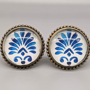 May include: Two decorative cabinet knobs with a blue and white floral design. The knobs are made of metal with a brass finish.