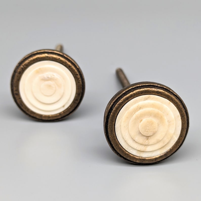 May include: Two antique-style cabinet knobs with a white, concentric circle design and a bronze metal base.