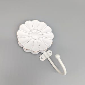 May include: White metal flower-shaped hook with a single hook arm. The hook is distressed and has a vintage look.