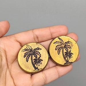May include: Two gold-coloured metal palm tree earrings. The palm trees are black and have a textured finish.