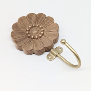 May include: A wooden flower-shaped wall hook with a gold metal hook. The flower is carved with a detailed design and has a brown finish.
