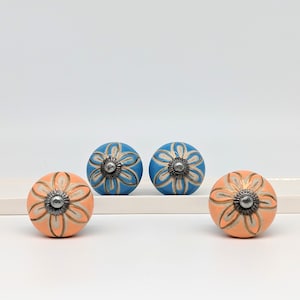 May include: Three ceramic knobs with floral designs. Two knobs are blue with white and gold accents, and one knob is peach with white and gold accents.
