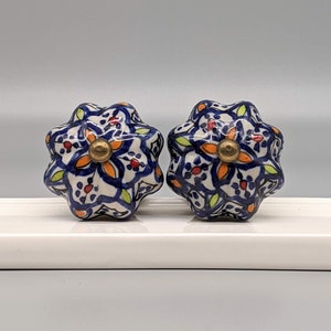 May include: Two blue and white ceramic knobs with a floral pattern and gold accents. The knobs have a starburst shape.