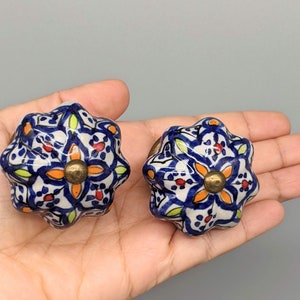 May include: Two blue and white ceramic knobs with intricate floral patterns and gold accents. The knobs have a raised, textured surface and are perfect for adding a touch of Moroccan style to furniture.