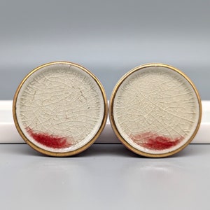 May include: Two white ceramic knobs with a gold rim and a red accent. The knobs have a crackled finish.