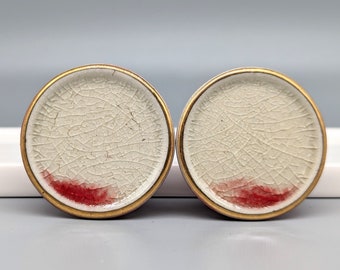 May include: Two white ceramic knobs with a gold rim and a red accent. The knobs have a crackled finish.