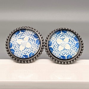 Könnte beinhalten: Zwei runde, silberfarbene, dekorative Schubladengriffe mit einem weißen und blauen Muster. Das Muster zeigt ein weißes, schneeflockenartiges Design auf blauem Hintergrund.