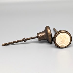 May include: Two antique bronze cabinet knobs with a white circular design. One knob has a threaded screw.