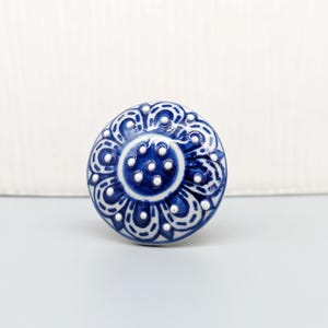 May include: A blue and white ceramic knob with a floral design. The knob has a raised center with white dots and a blue border.
