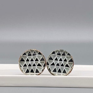 May include: A pair of round, black and white patterned earrings with a silver rim. The pattern is a geometric design of triangles.