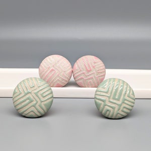 May include: Three ceramic knobs with a geometric pattern. Two are light green with a white pattern and one is pink with a white pattern.