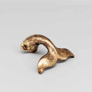 May include: A gold-coloured metal whale tail door pull. The tail is curled up and the fin is spread out.