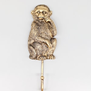 May include: Gold monkey hook with a textured finish. The monkey is sitting with its hand on its chin. The hook is attached to the monkey's back.