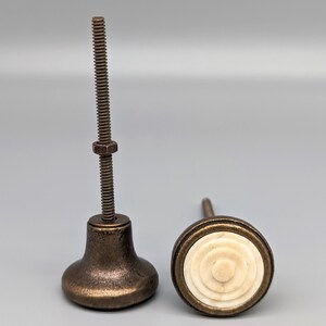 May include: Two antique bronze cabinet knobs with a white bone inlay. The knob on the left has a screw and the knob on the right has a round bone inlay.