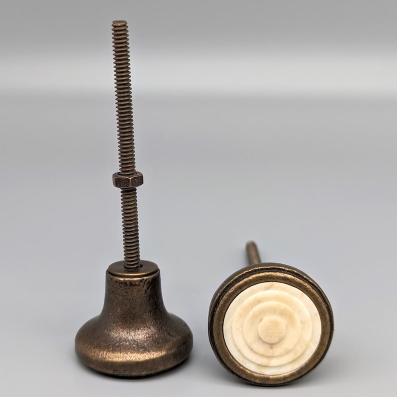 May include: Two antique bronze cabinet knobs with a white bone inlay. The knob on the left has a screw and the knob on the right has a round bone inlay.