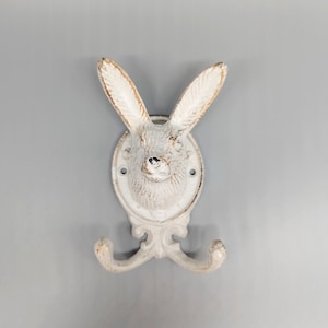 May include: White ceramic bunny rabbit wall hook with two hooks. The bunny has a distressed white finish and a cute, whimsical design.